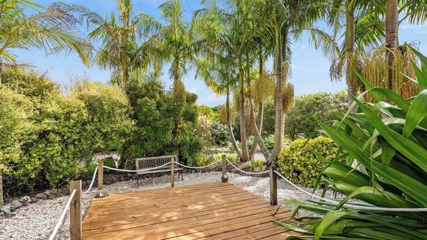 A wooden deck surrounded by lush greenery and palm trees. - Cozy 1 bedroom unit nestled in a lush sub tropical garden located in Kerikeri. (Kerikeri)