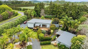 A modern house with a large garden, surrounded by lush greenery and hills in the background. - Cozy 1 bedroom unit nestled in a lush sub tropical garden located in Kerikeri. (Kerikeri)