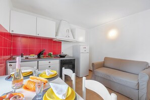 Eine moderne Küche mit weißen Schränken, roten Fliesen und einem beigen Sofa in einem Wohnbereich.