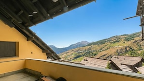 Ein Balkon mit Blick auf eine gebirgige Landschaft, Holzbalken und einer gelben Wand.
