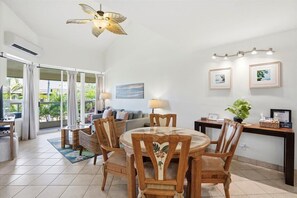 Un coin repas avec une table ronde et des chaises, un ventilateur de plafond et une vue à travers les portes vitrées.