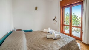 A hotel room with a large bed, a window with a view of trees, and a small table with a bottle. - Tramonto D'Oro Apartment Near The Beach, Porto Cesareo, Italy (Porto Cesareo)