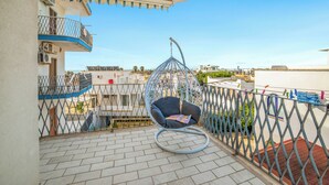 A balcony with a hanging chair, a metal fence, and a view of buildings in the distance. - Tramonto D'Oro Apartment Near The Beach, Porto Cesareo, Italy (Porto Cesareo)