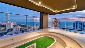 Ein modernes Interieur mit einer gebogenen Sitzgruppe, großen Fenstern mit Blick auf die Stadt und einem dekorativen, geometrischen Wandbild.