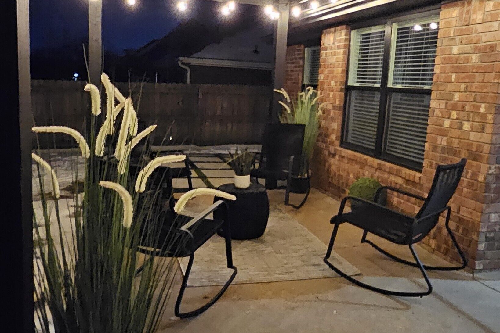 An outdoor patio with two black rocking chairs, a small table, and potted plants.