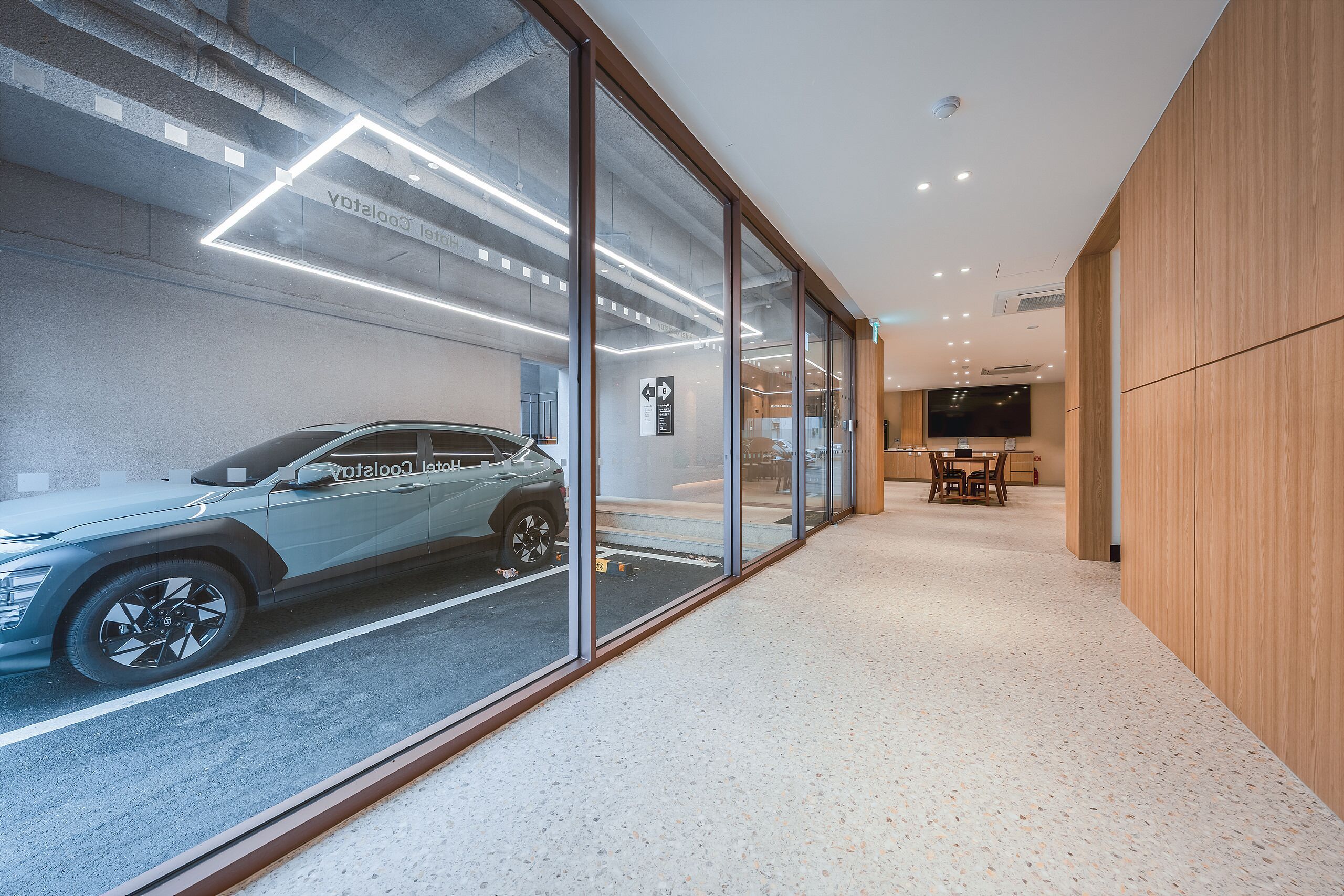 Un interior moderno con un coche exhibido a través de una pared de vidrio, una pared de madera e iluminación empotrada en el techo.