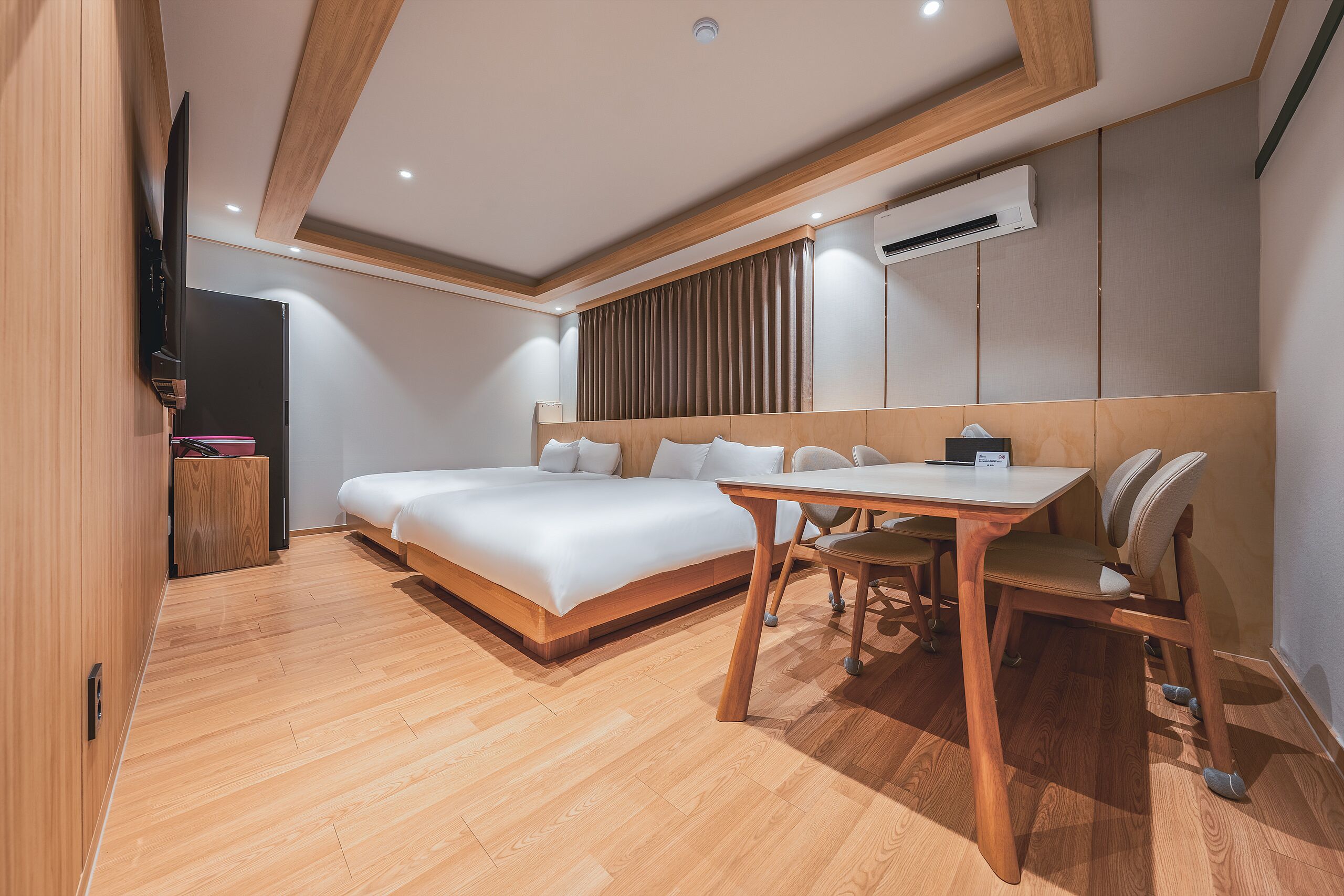 A modern hotel room with a large bed, a dining table, and a TV.