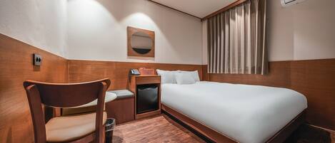 A hotel room with a bed, a chair, a small table with a phone, a mirror, and a window with curtains.