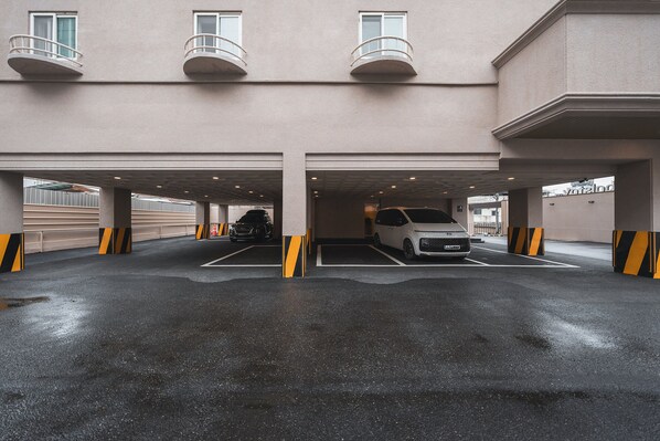 Un área de estacionamiento techada con dos autos estacionados, un edificio con balcón y un letrero que dice 'votelogo'.