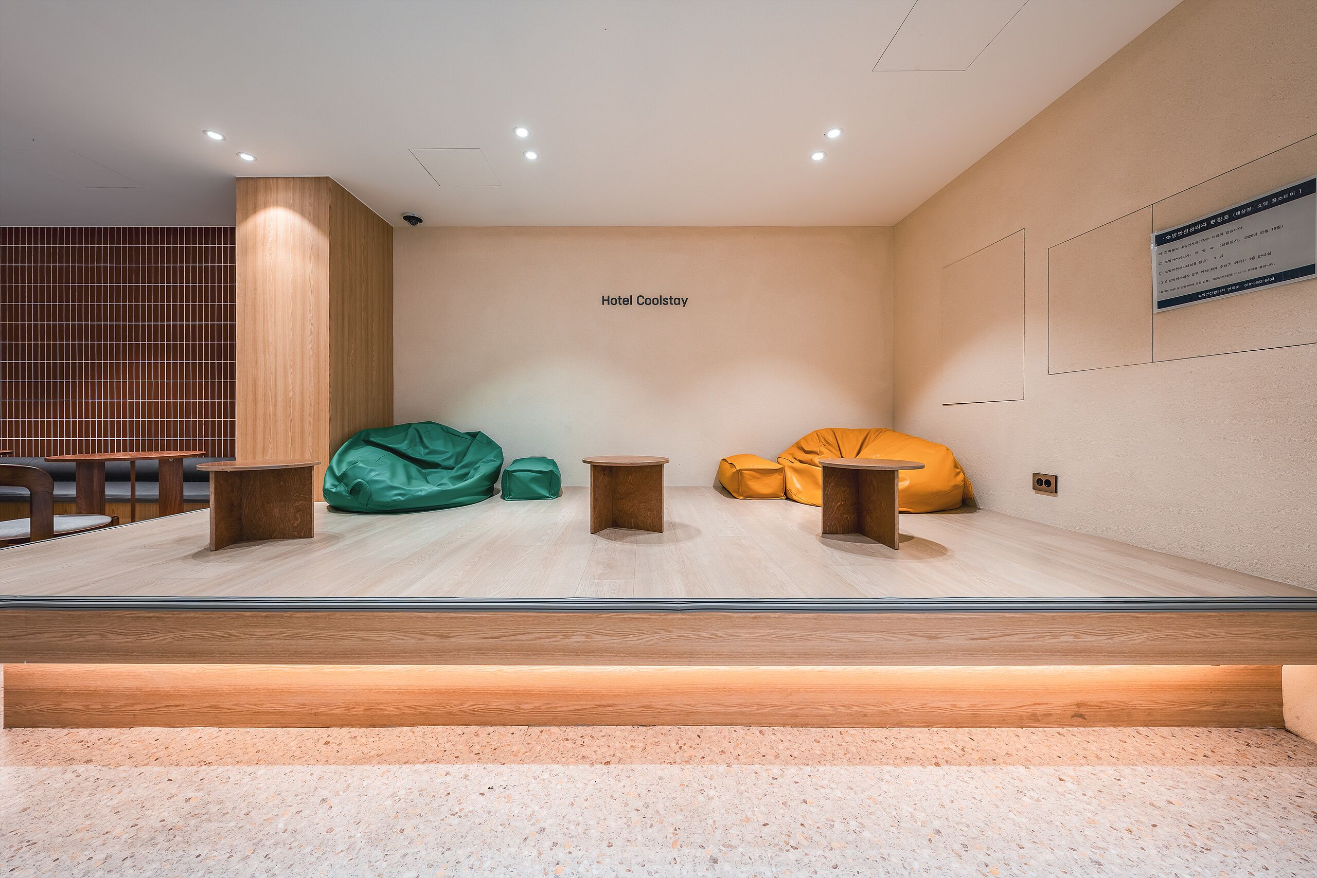 A modern hotel lobby with a seating area featuring green and yellow bean bags, wooden tables, and a wooden partition wall.