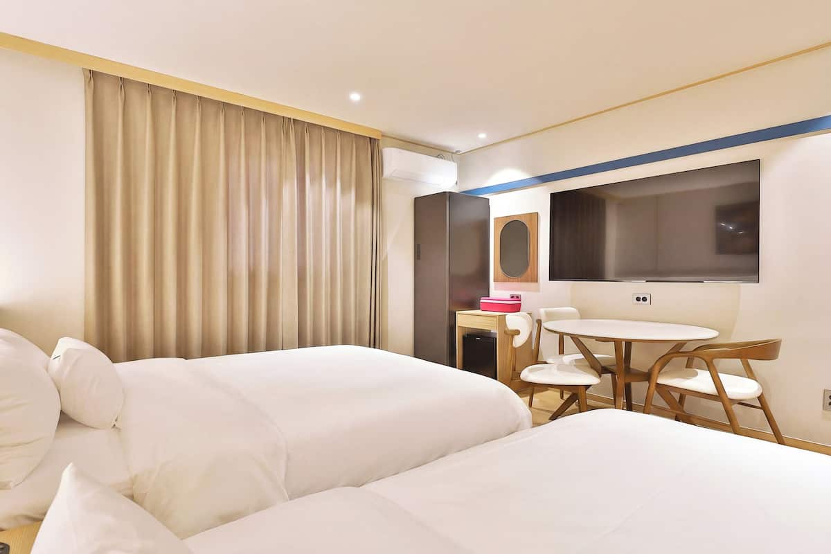 A hotel room with two beds, a desk with a chair, a small table, and a mirror.