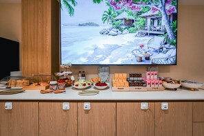 En frukostbuffé med ett varierat utbud av mat och en tropisk strandscen på väggen.