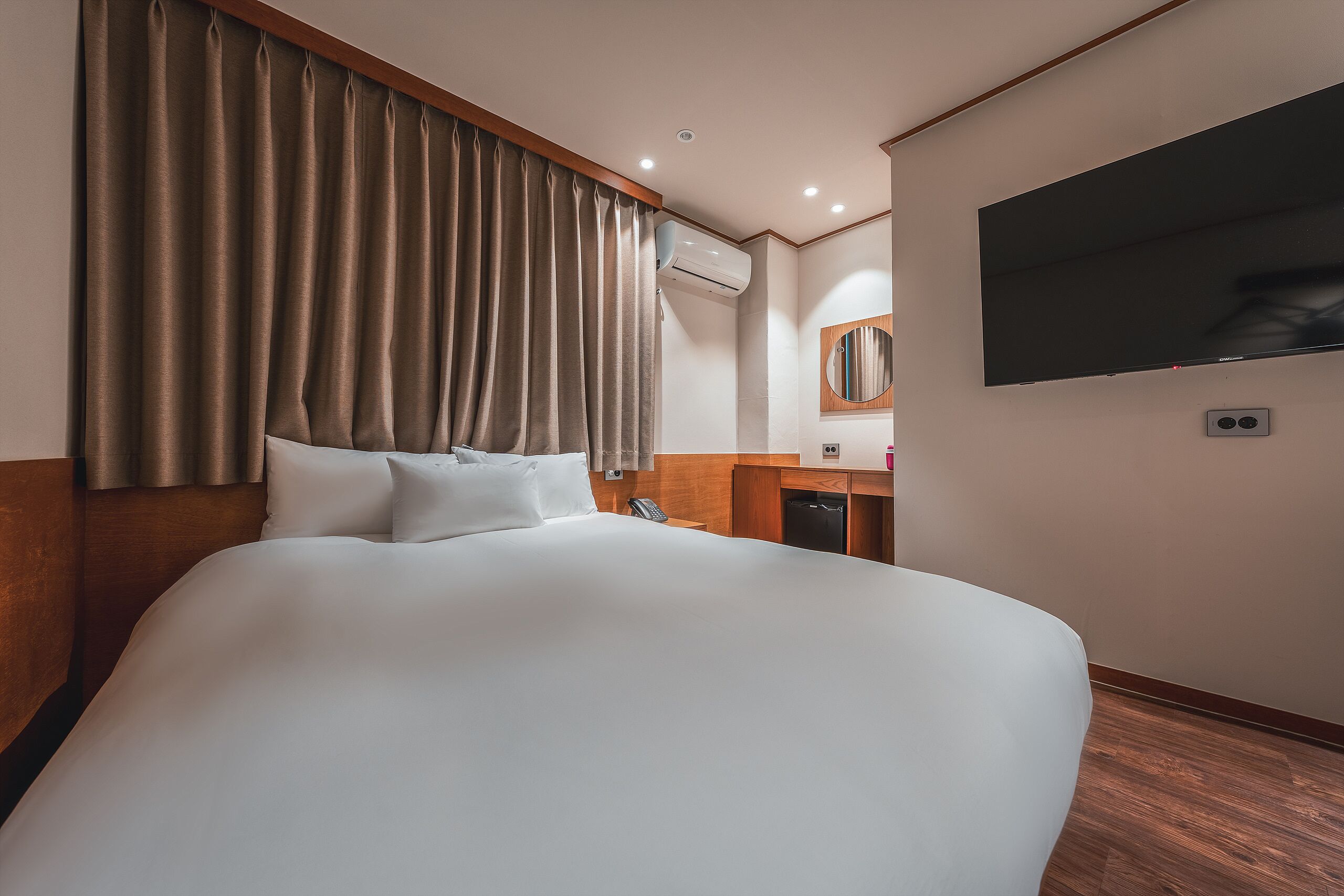 A hotel room with a large bed, a flat-screen TV mounted on the wall, a wooden headboard, and a built-in wardrobe.