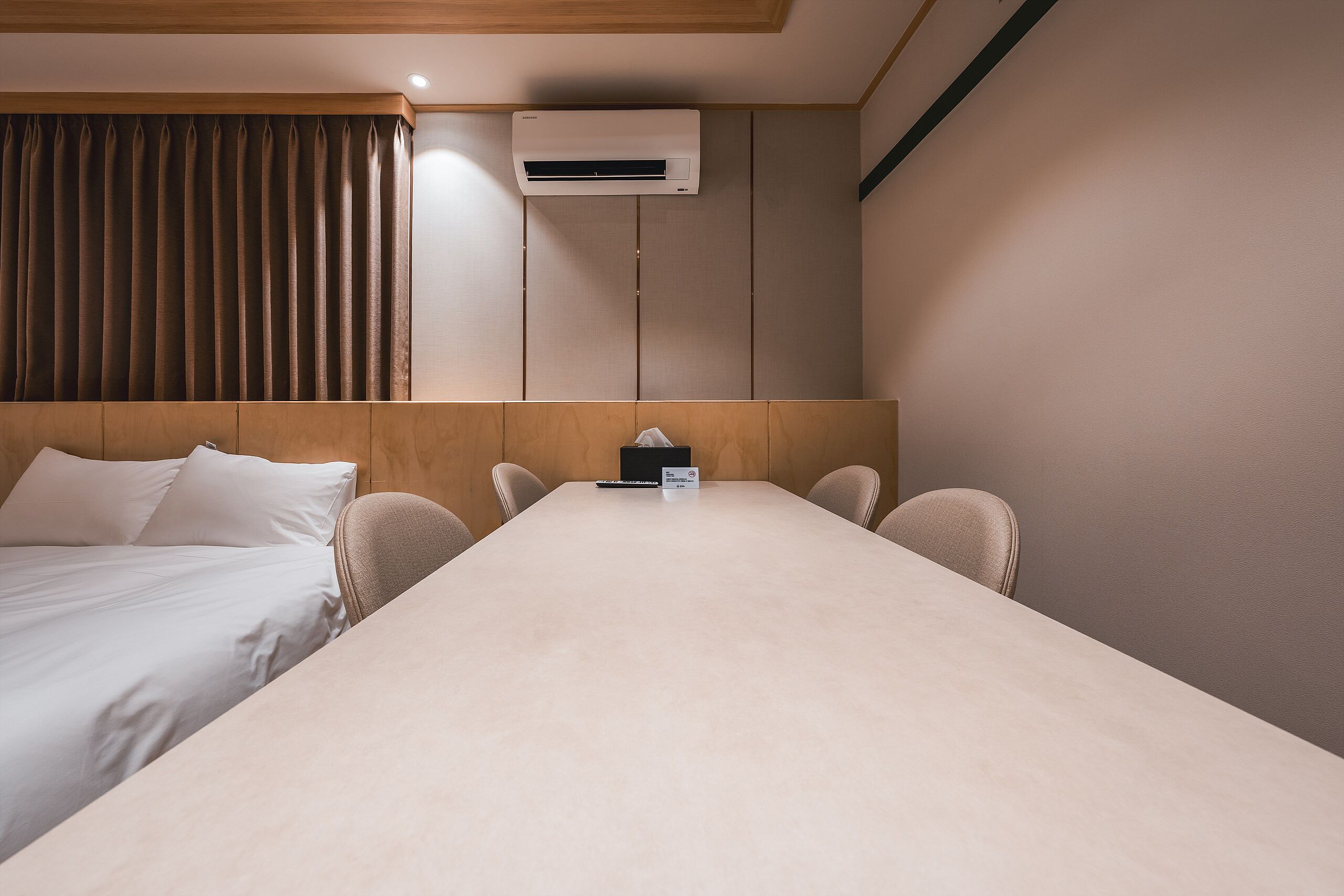 Habitación de hotel con cama, una mesa, sillas, equipo de aire acondicionado y una cortina.