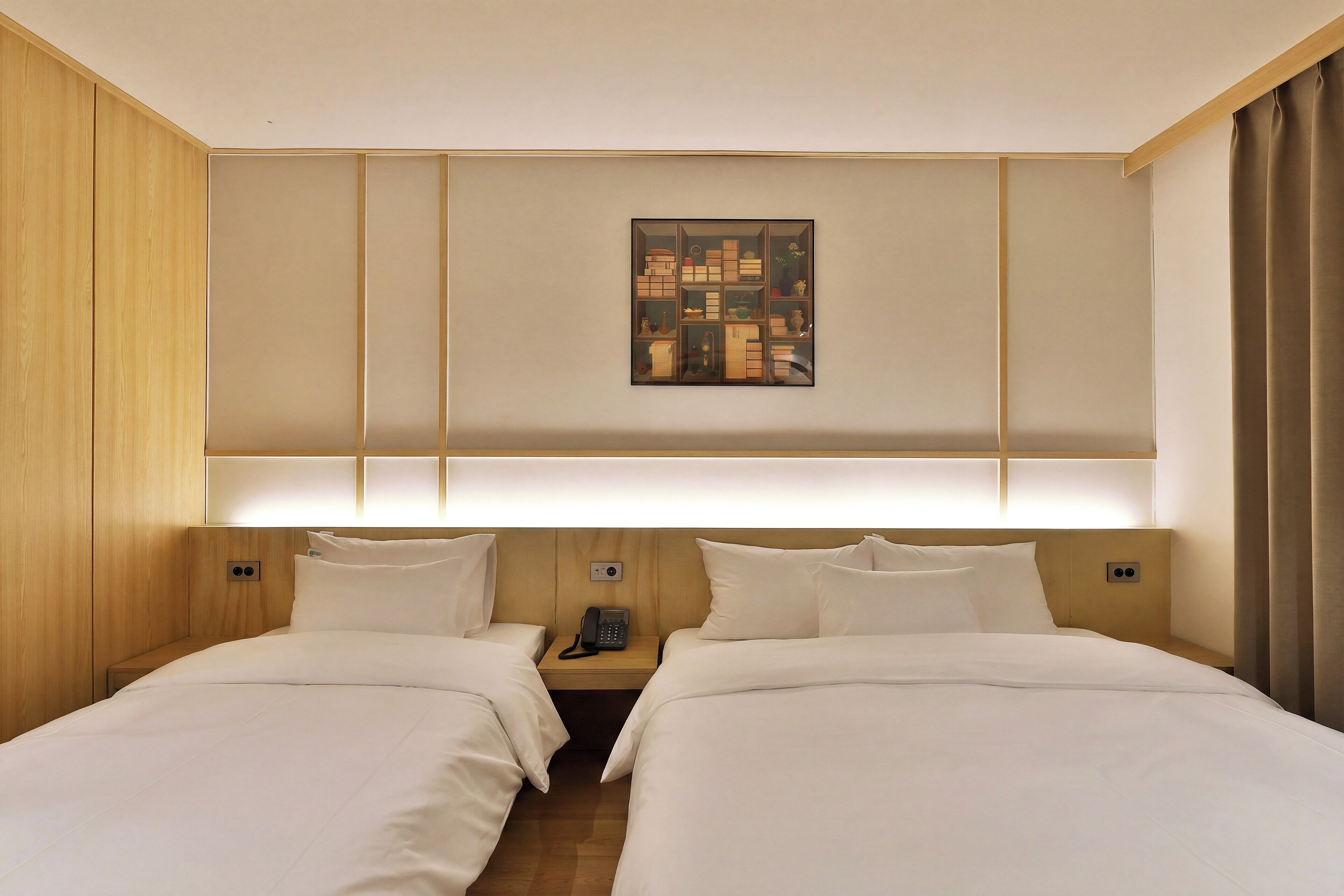 A hotel room with two beds, a bedside table with a phone, and a wall-mounted artwork.