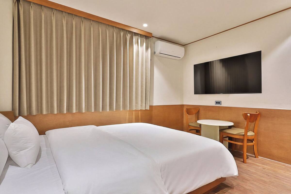 A hotel room with a bed, a TV mounted on the wall, a small table, and a chair.