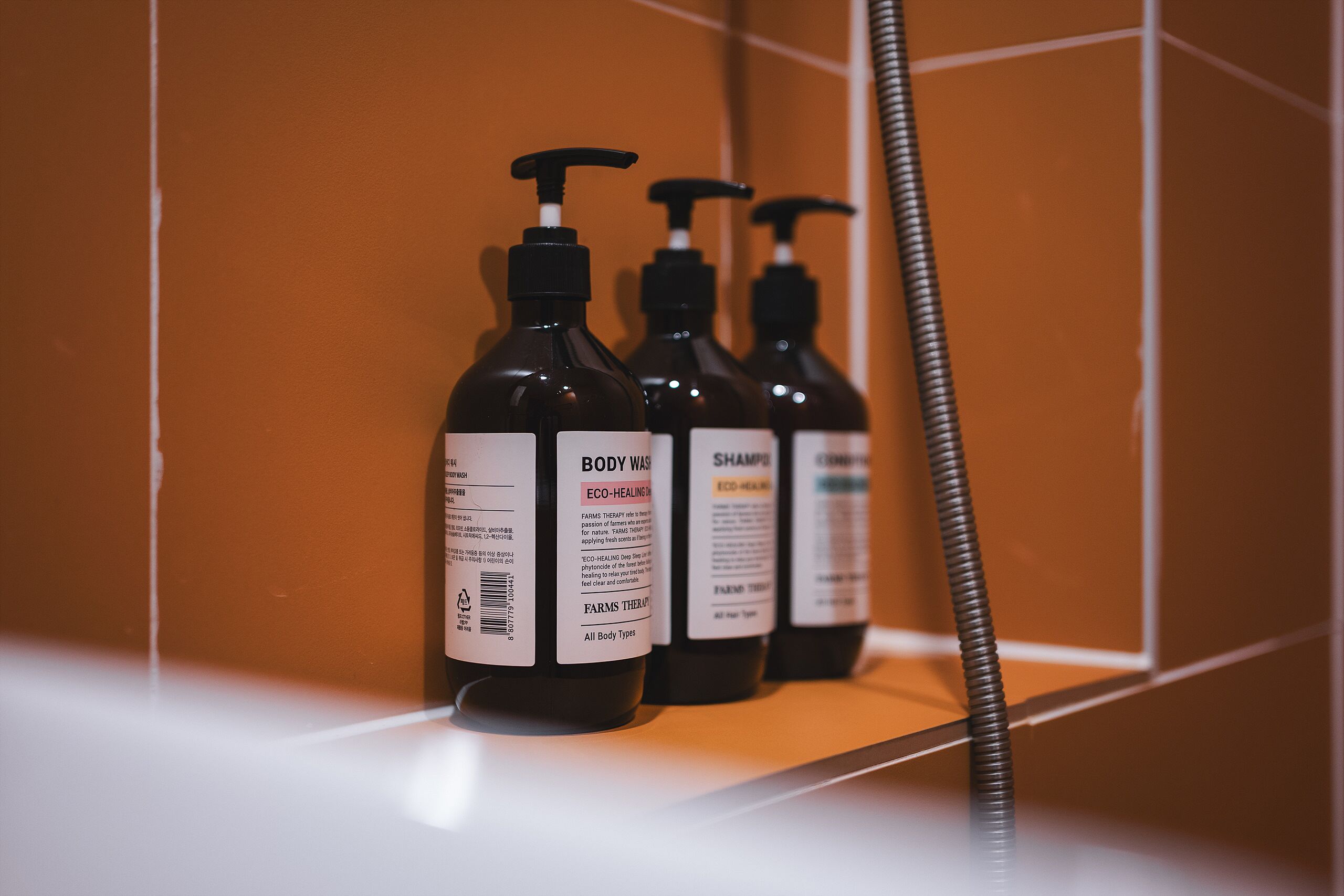 Trois bouteilles de gel douche sont posées sur une étagère dans une salle de bain, sous une tringle à rideau de douche.