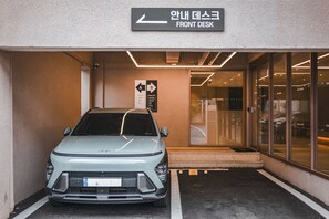A parking area with a car, a sign for a front desk, and a building entrance. - Hotel Coolstay Gimcheon (Gimcheon)