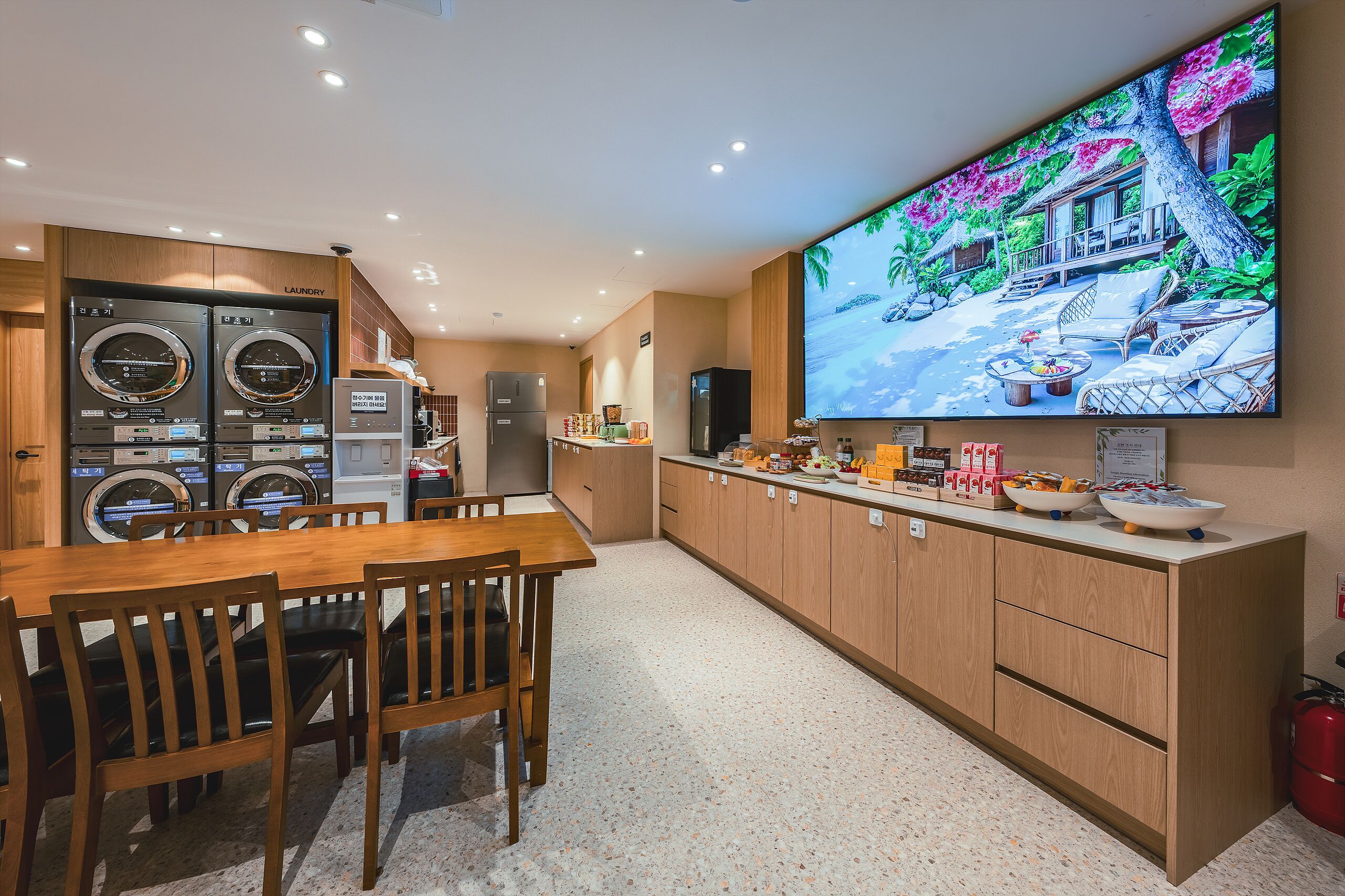 A modern kitchen with built-in appliances, a dining area with wooden furniture, and a large flat-screen TV displaying a tropical scene.