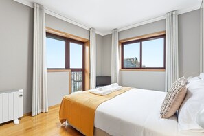 A hotel room with a large bed, two windows, a radiator, and a view of buildings. - GuestReady - Gaia Gardens Apt 4 (Vila Nova de Gaia)