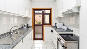 Een moderne keuken met witte kastjes, granieten aanrecht, een inbouwoven en een raam met uitzicht op een gebouw.