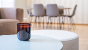 Een moderne woonkamer met een ronde witte tafel, een donkere glazen object op de tafel en een zithoek met stoelen en een bank op de achtergrond.