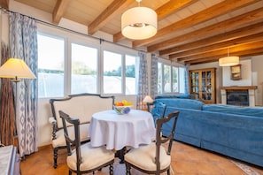 A cozy room with a wooden ceiling, a blue sofa, a round table with a white tablecloth, and a fireplace. - CAN SOMNI - Charming house 10 minutes from the beach with private pool and free WiFi (Ses Salines)