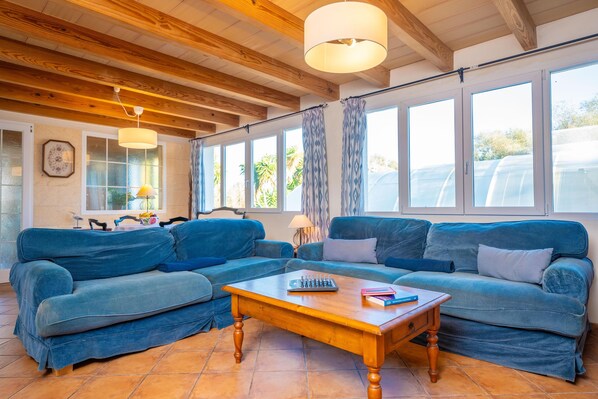 Uma sala de estar com teto de madeira, grandes janelas, um sofá azul e uma mesa de centro de madeira.