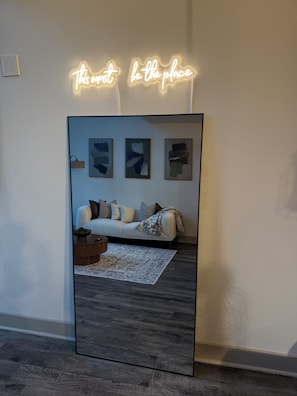 A modern living room with a large mirror reflecting a sofa, cushions, and abstract art on the wall. - Modern Organic Luxury Loft - Downtown Atlanta (Atlanta)