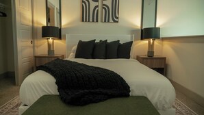 Una cama bien hecha con un edredón negro, dos lámparas de noche y un espejo en la pared.