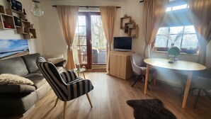 A living room with a sofa, a striped armchair, a small table, a television, and a window with curtains. - Suite by the forest (Bad Sachsa)