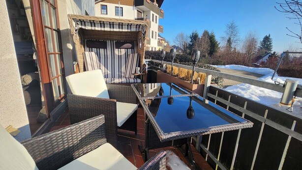 A balcony with wicker furniture, a glass table, and a view of a snowy landscape. - Suite by the forest (Bad Sachsa)