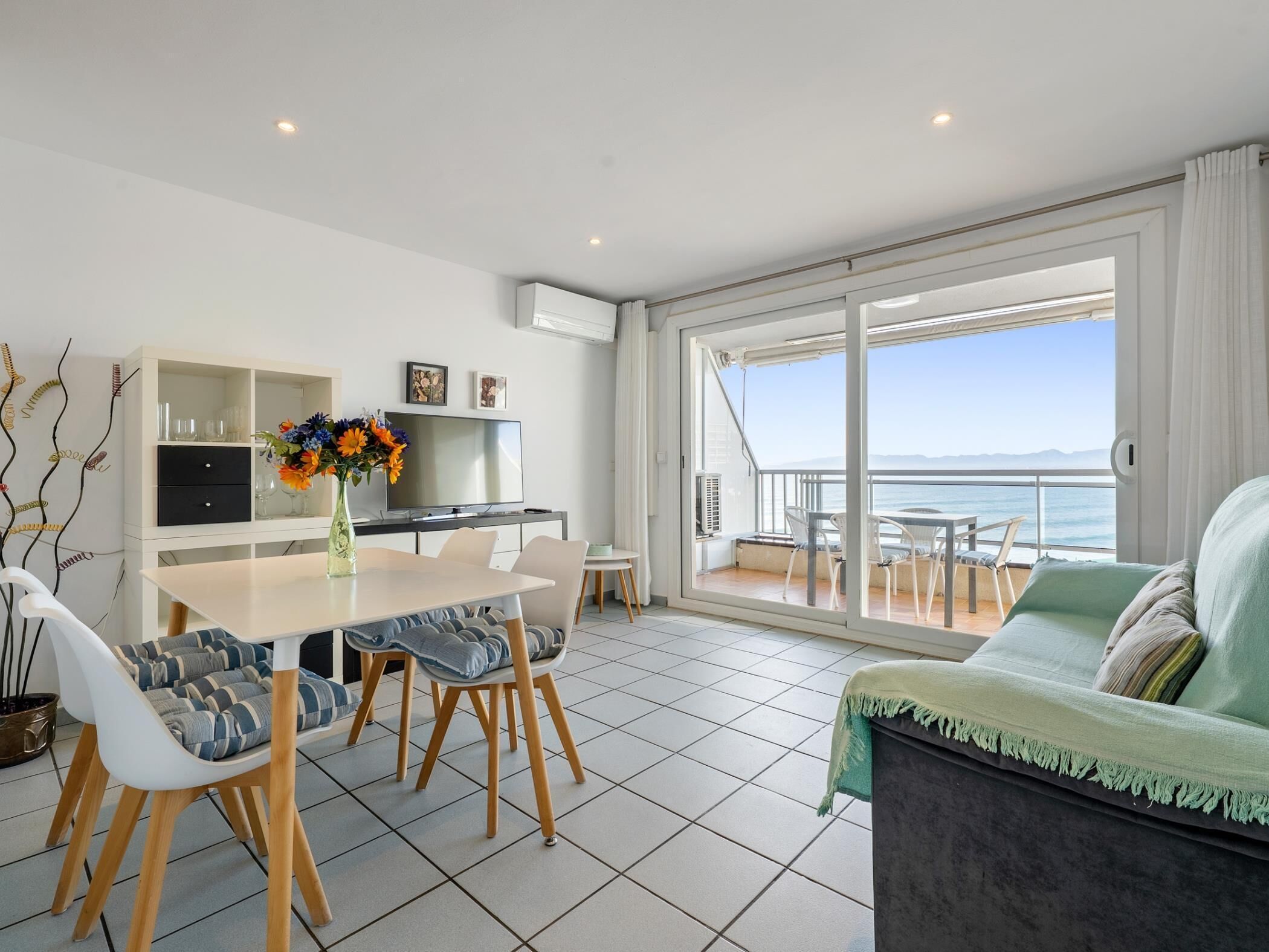 A modern living room with a balcony, a dining area with a table and chairs, and a TV on a cabinet.