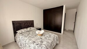 A bedroom with a bed, a dark headboard, a nightstand, a wardrobe, and a door.