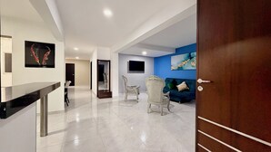 A modern living room with a blue accent wall, a wooden door, and a flat-screen TV mounted on the wall.