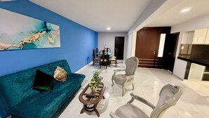 A modern living room with a blue wall, a green sofa, a coffee table, and a dining area in the background.
