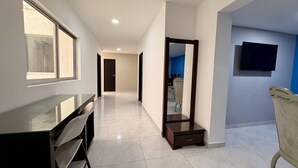 A hallway with a desk, a mirror, and a television on the wall.