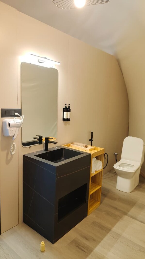 A modern bathroom with a large mirror, a black sink, and a white toilet.