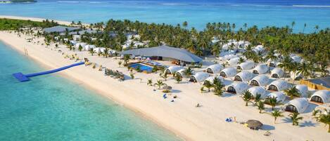 Un resort con alojamientos de forma abovedada, una playa y una zona de piscina.