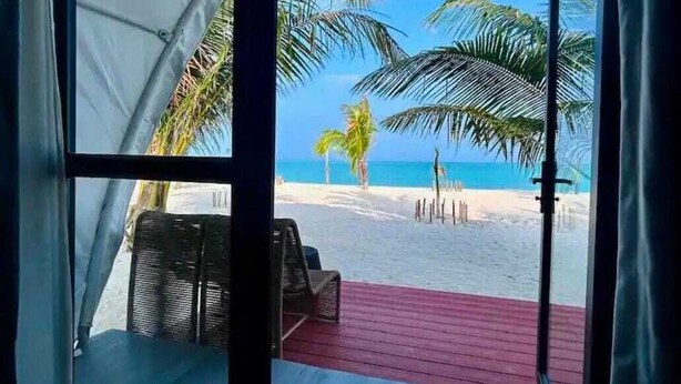 Une vue sur la plage depuis une chambre dotée d’une porte-fenêtre coulissante, d’une terrasse rouge et d’un auvent blanc.
