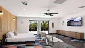 Ein modernes Hotelzimmer mit Bett, Deckenventilator, großem Fenster mit Blick auf Grünflächen und einem flachbildfernseher an der Wand.