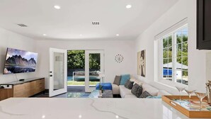 Ein modernes Wohnzimmer mit Fernseher, Sofa, Couchtisch und Blick auf einen Pool.