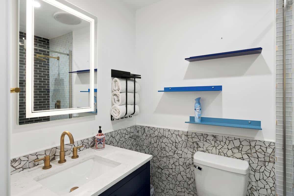Une salle de bain avec un lavabo blanc, un miroir, des toilettes et des étagères bleues.