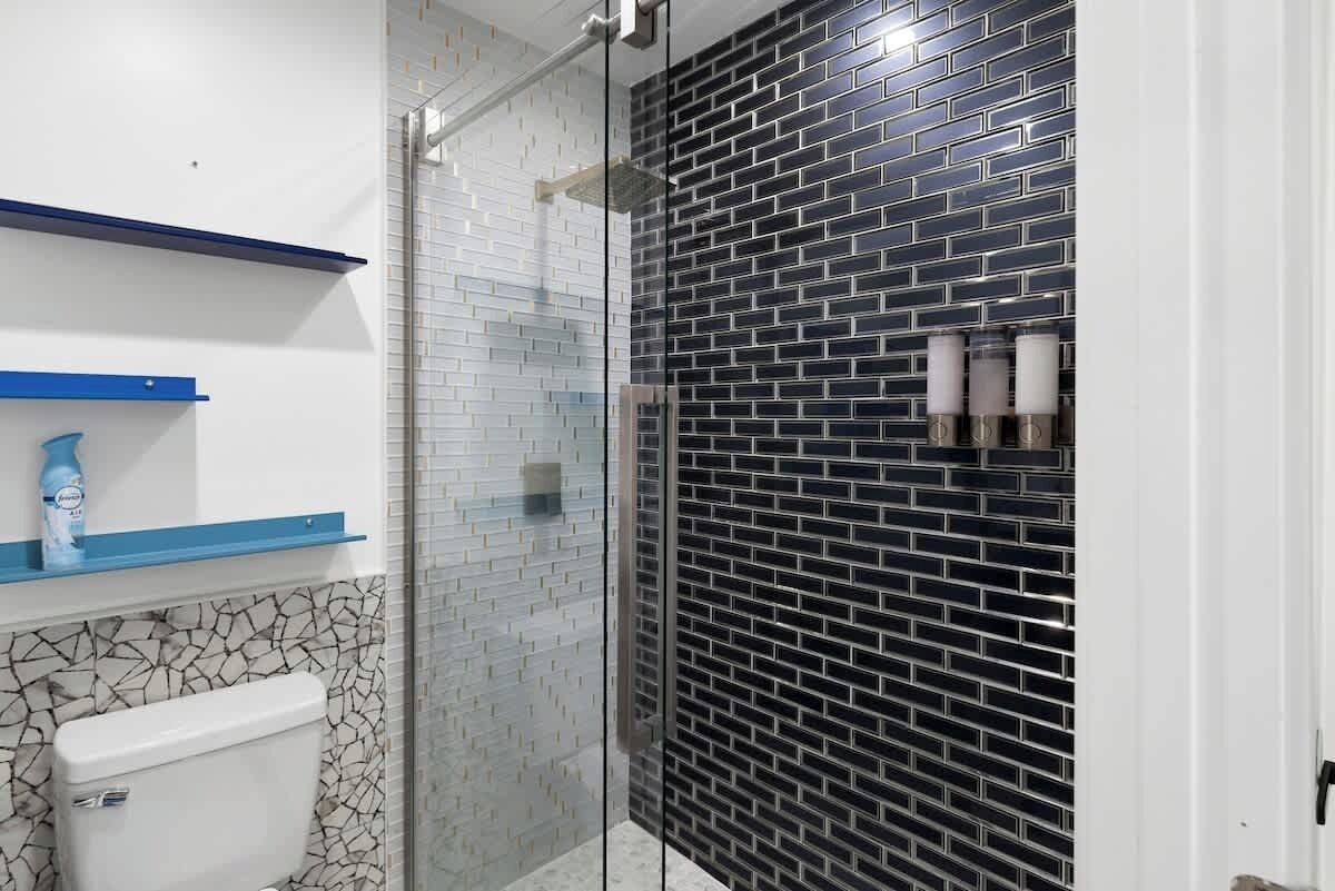 Casa de banho com sanita, chuveiro com portas de vidro e parede revestida a azulejos preto e branco.