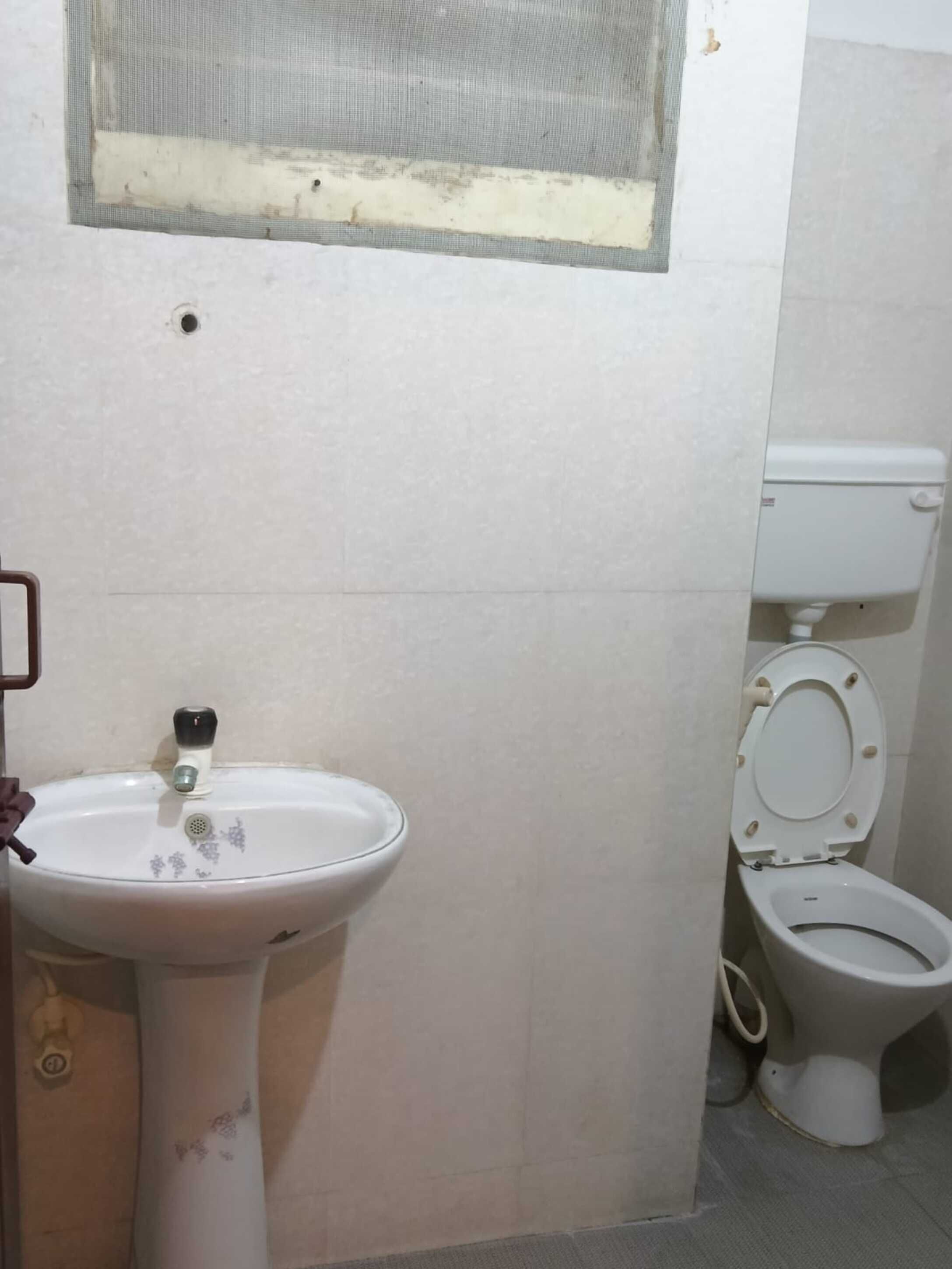 A bathroom with a white sink, toilet, and a window with a mesh screen.