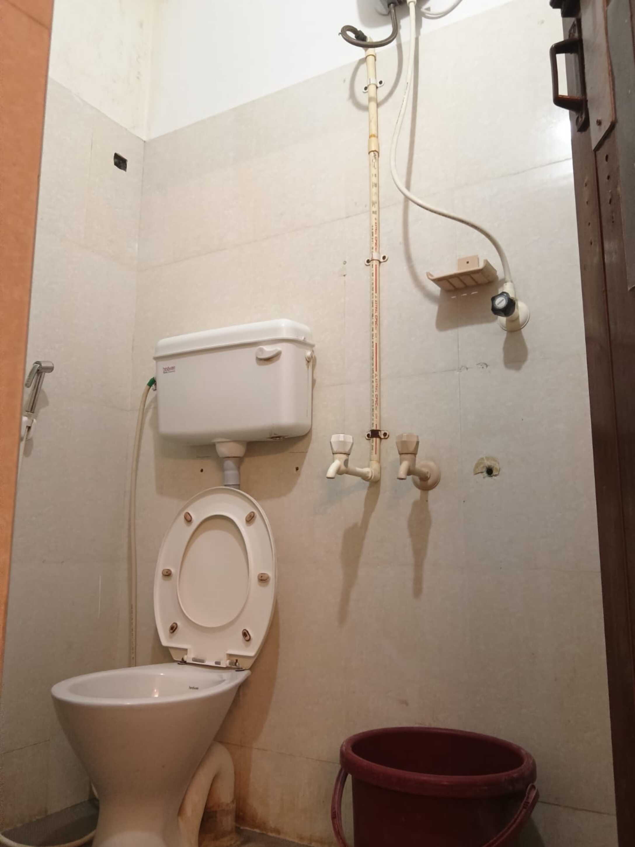 A small bathroom with a toilet, a bidet, and a red bucket.