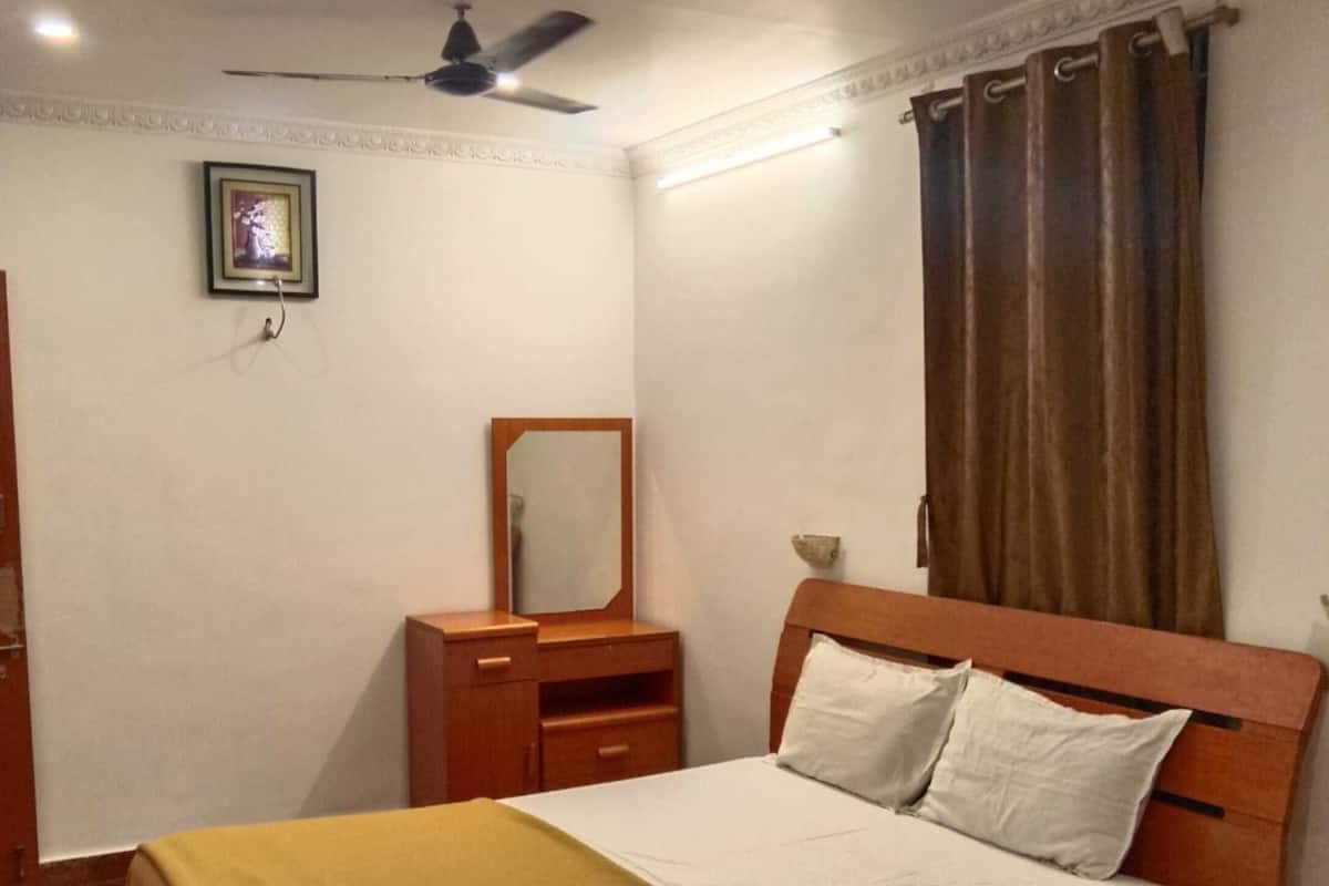 Un dormitorio con cama, mesita de noche, espejo, ventilador de techo y ventana con cortinas.