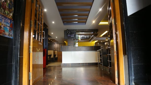 A hotel lobby with a reception desk, a wooden door frame, and a tiled floor. - Hotel Grand International (Erode)