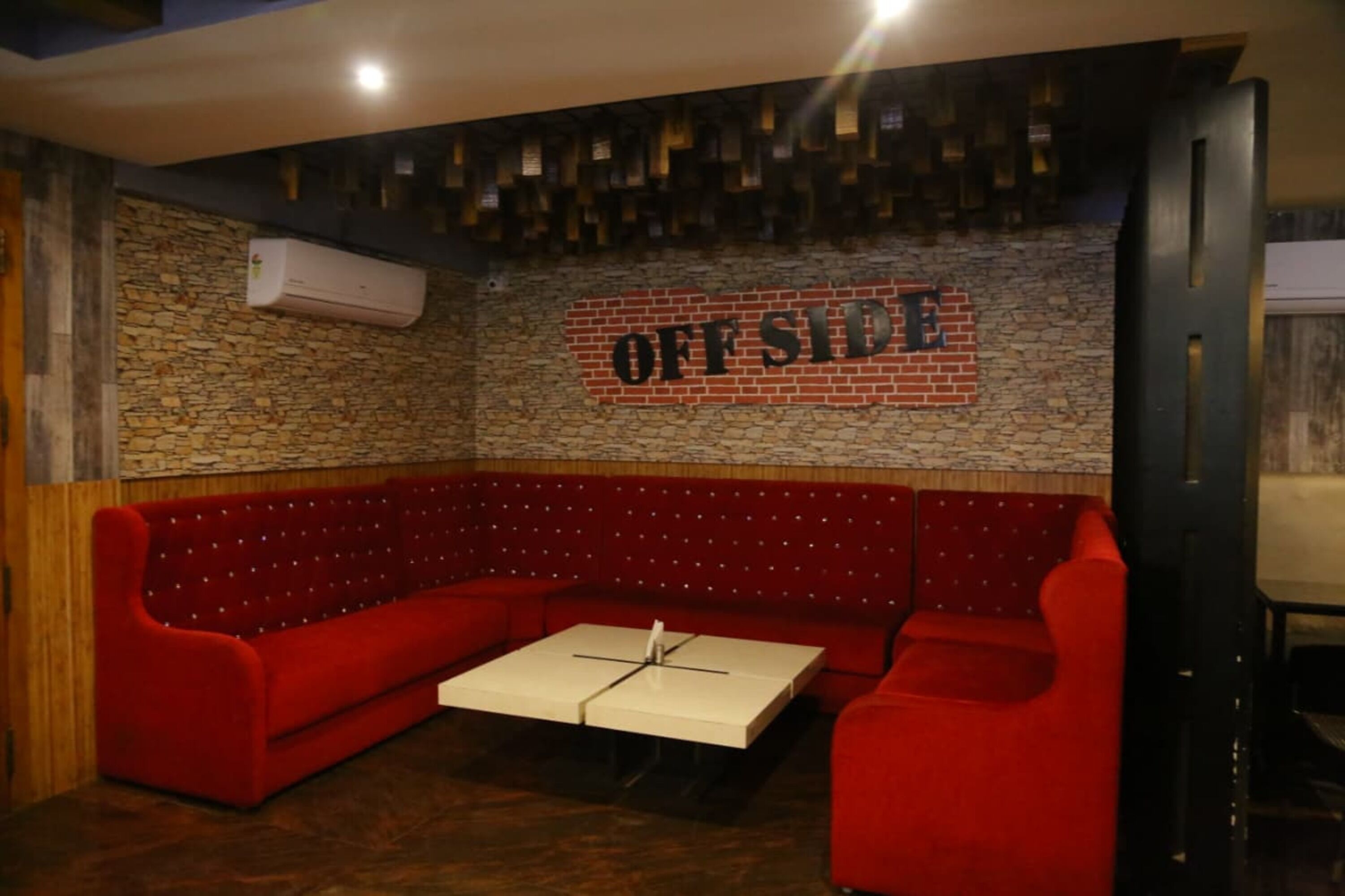 A red upholstered booth with a white table in the center, a brick wall, and a sign that reads "OFFSIDE".