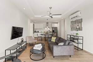 Ein modernes Wohnzimmer mit einer Couch, einem Couchtisch, einem Fernseher und einem Essbereich mit Stühlen und einem Tisch.